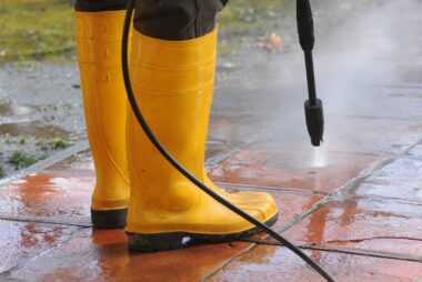 person-wearing-yellow-rubber-boots-with-high-pressure-water-nozzle-cleaning-the-dirt-in-the-tiles